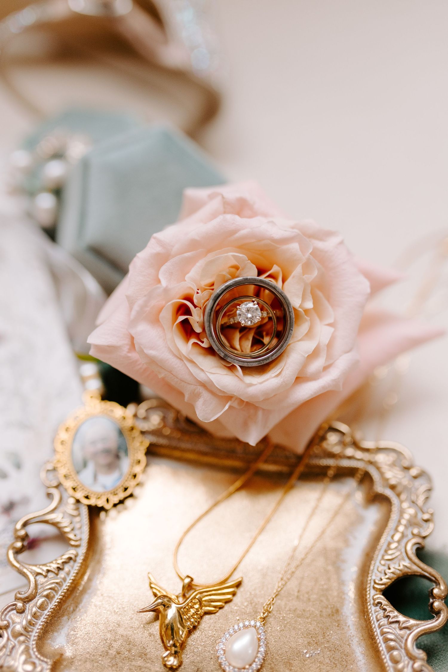 Wedding rings nestled in a blush pink rose with vintage jewelry and golden decorative elements on an ornate tray.