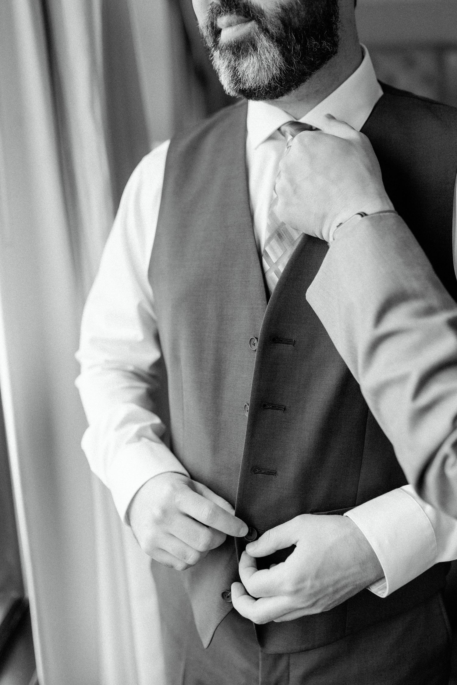 Close-up of a groom adjusting his tie and vest while getting ready for the wedding ceremony.