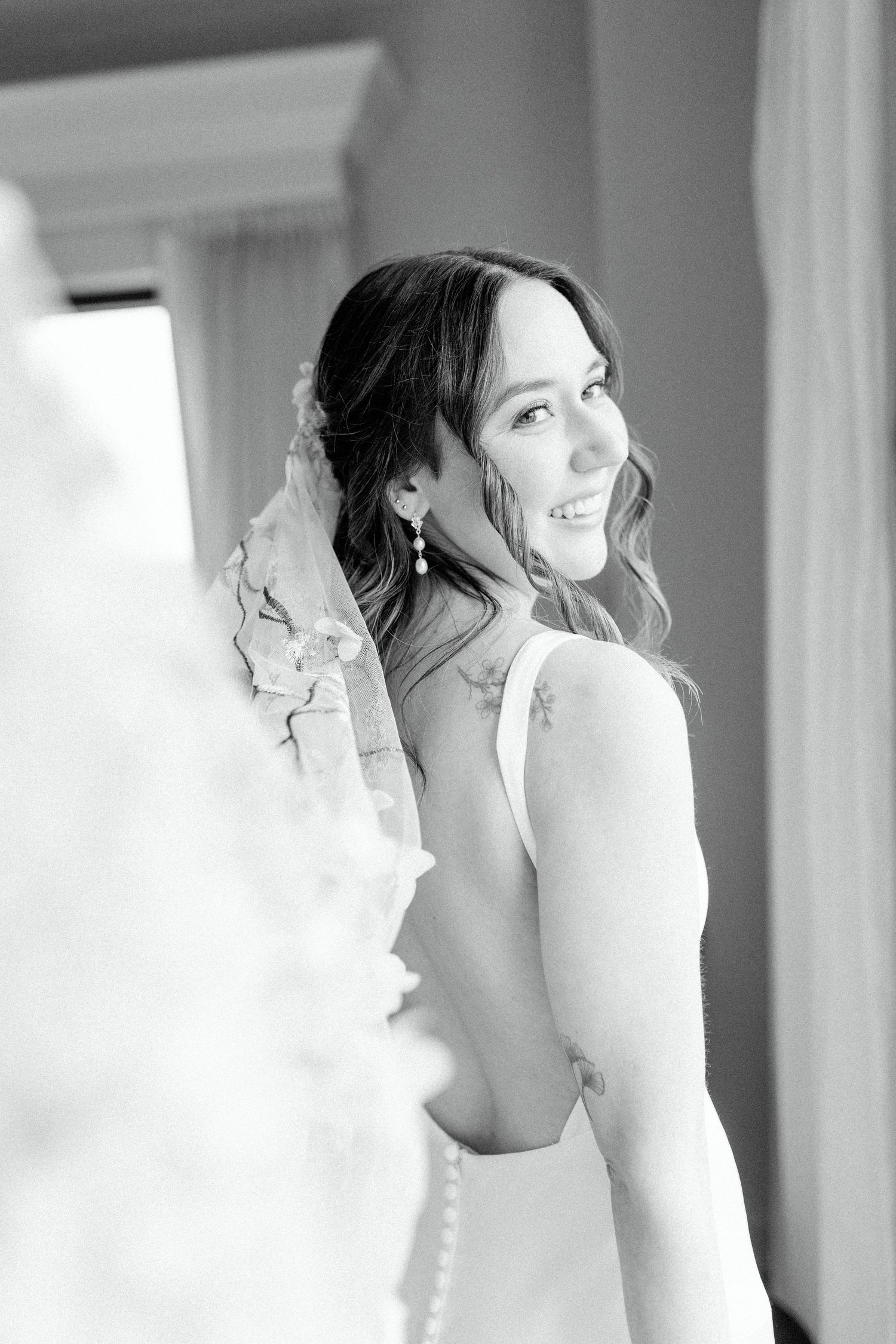 A classic black and white photograph of a bride in a backless wedding gown looking over her shoulder.