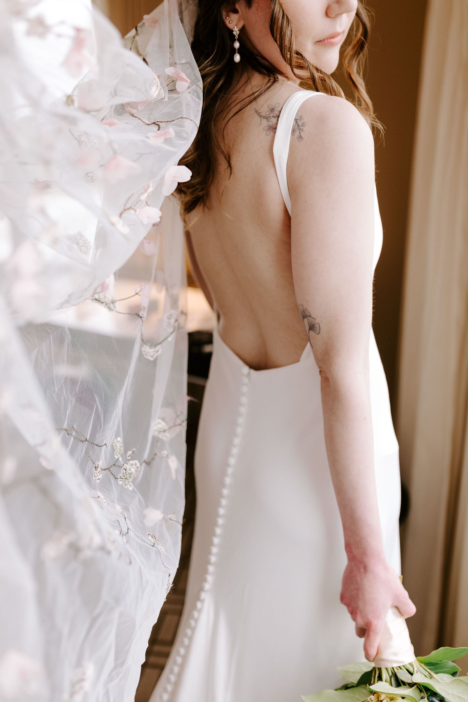 Elegant white wedding dress with delicate button details and open back design shown in warm natural lighting.