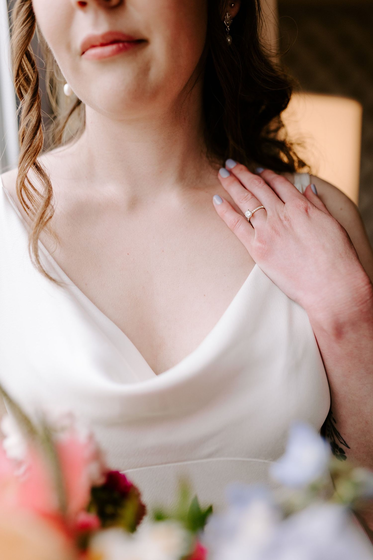 Close-up detail of an elegant white wedding dress with a cowl neckline and floral accents.