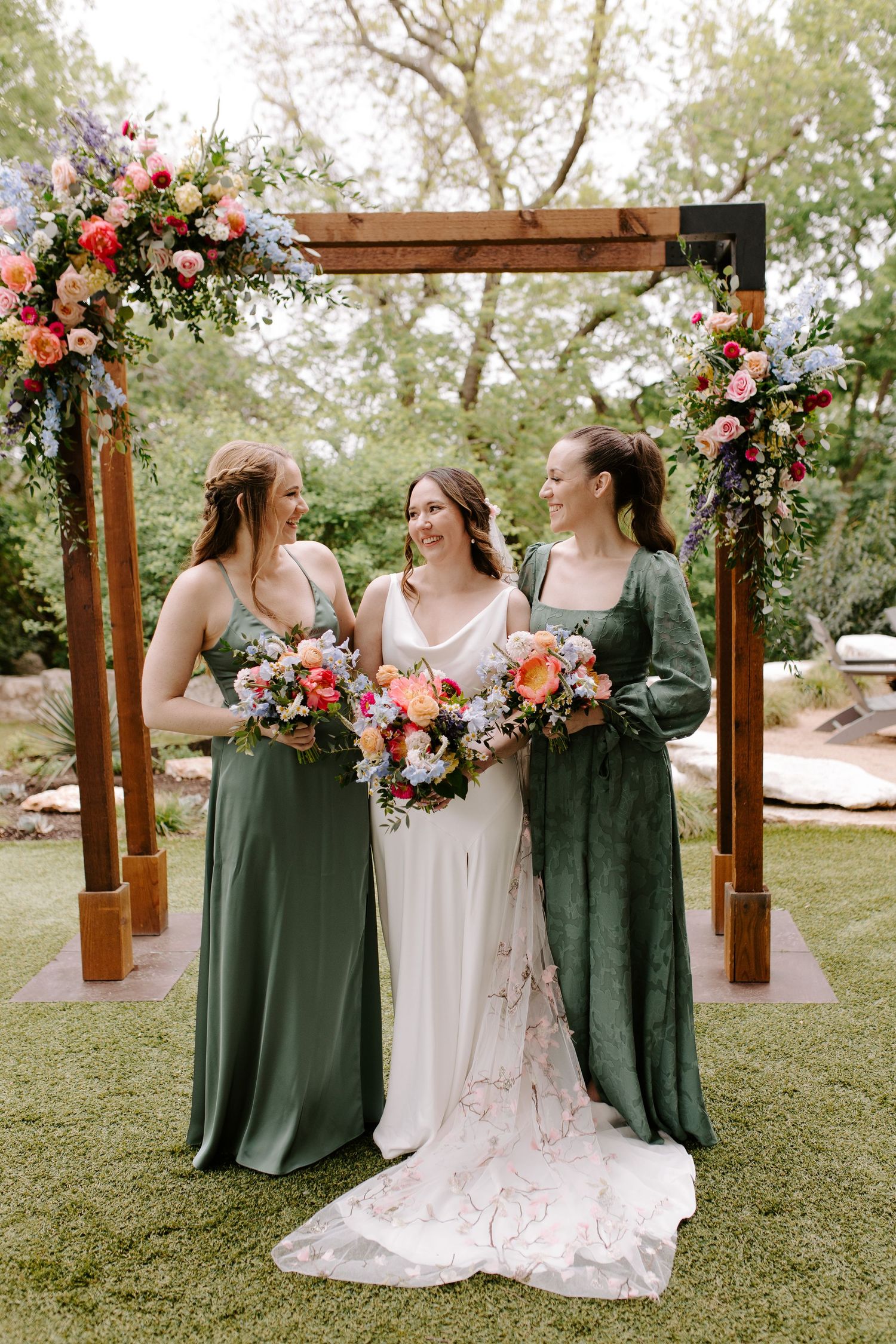 Rustic wooden arch adorned with coral and pink floral arrangements for an outdoor wedding ceremony.