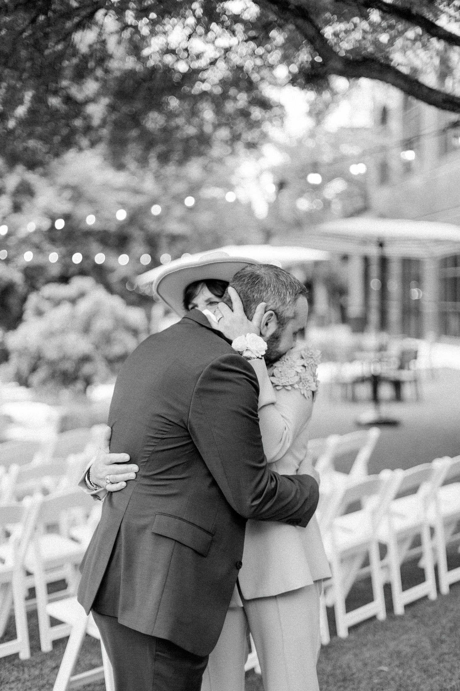 A touching black and white moment of two people embracing at an outdoor wedding ceremony.