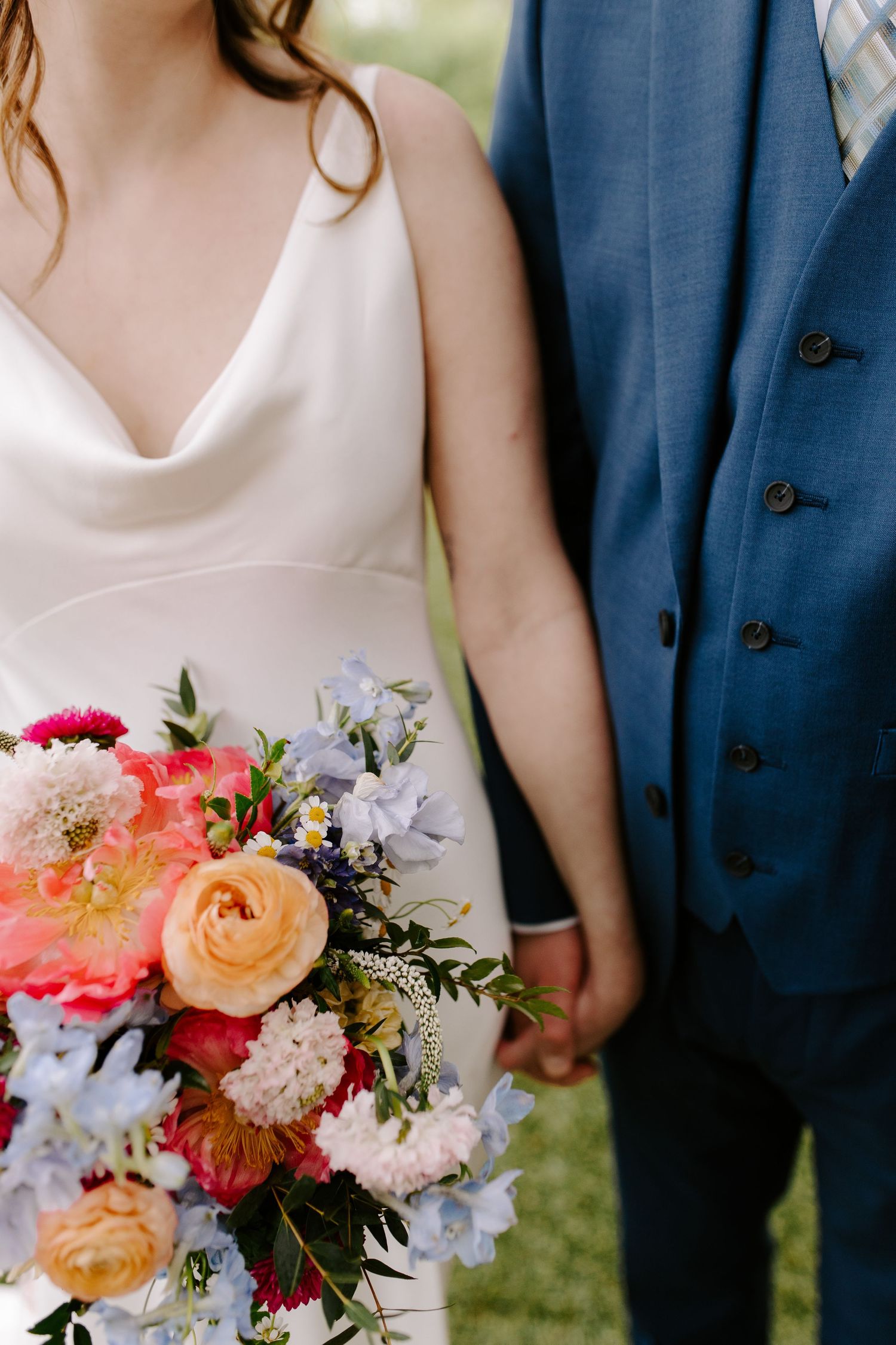 Close-up of wedding couple holding vibrant coral and peach floral bouquet.
