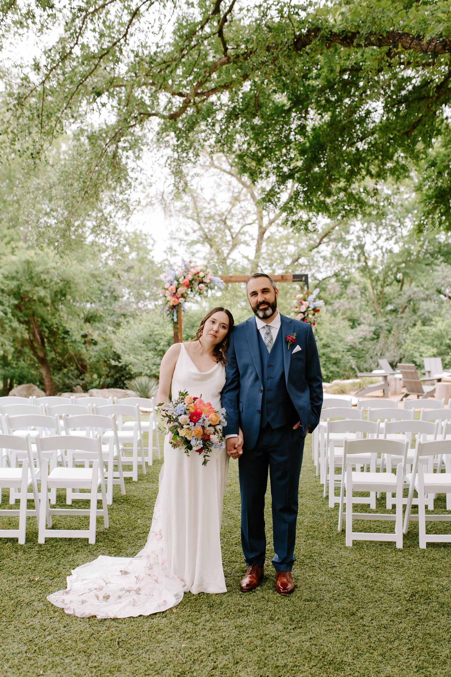 Happy newlyweds celebrate their outdoor garden wedding with rows of white chairs and lush greenery in the background.