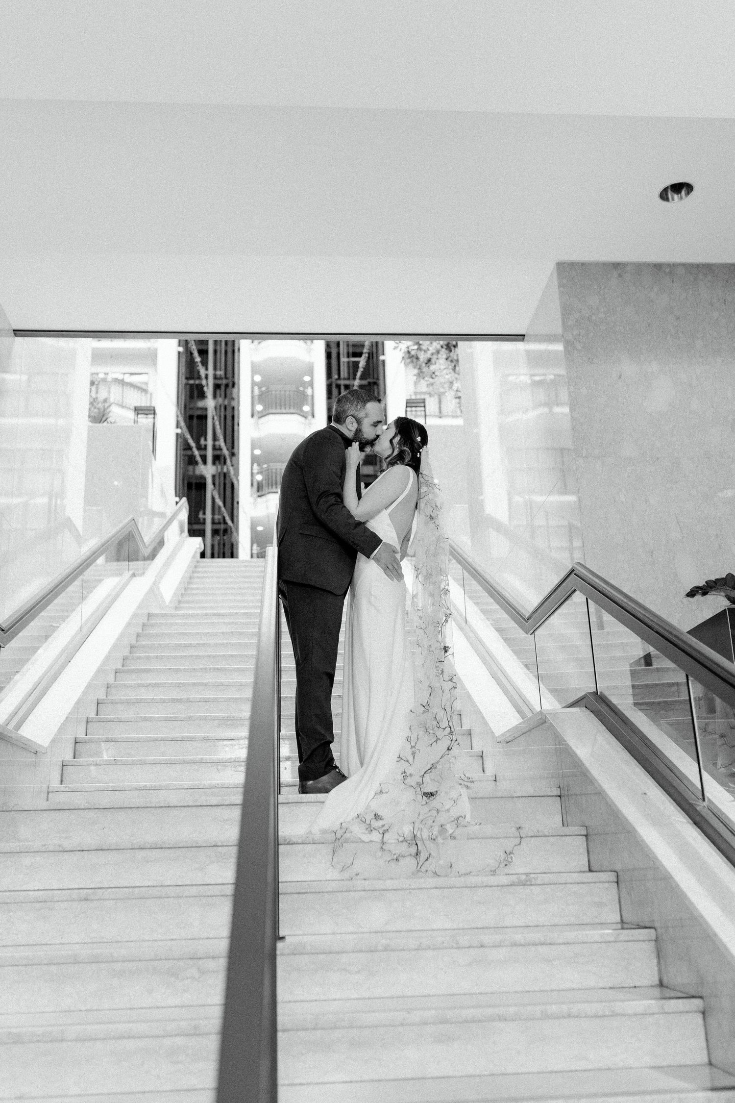Wedding couple ascending white marble stairs in an elegant indoor venue.