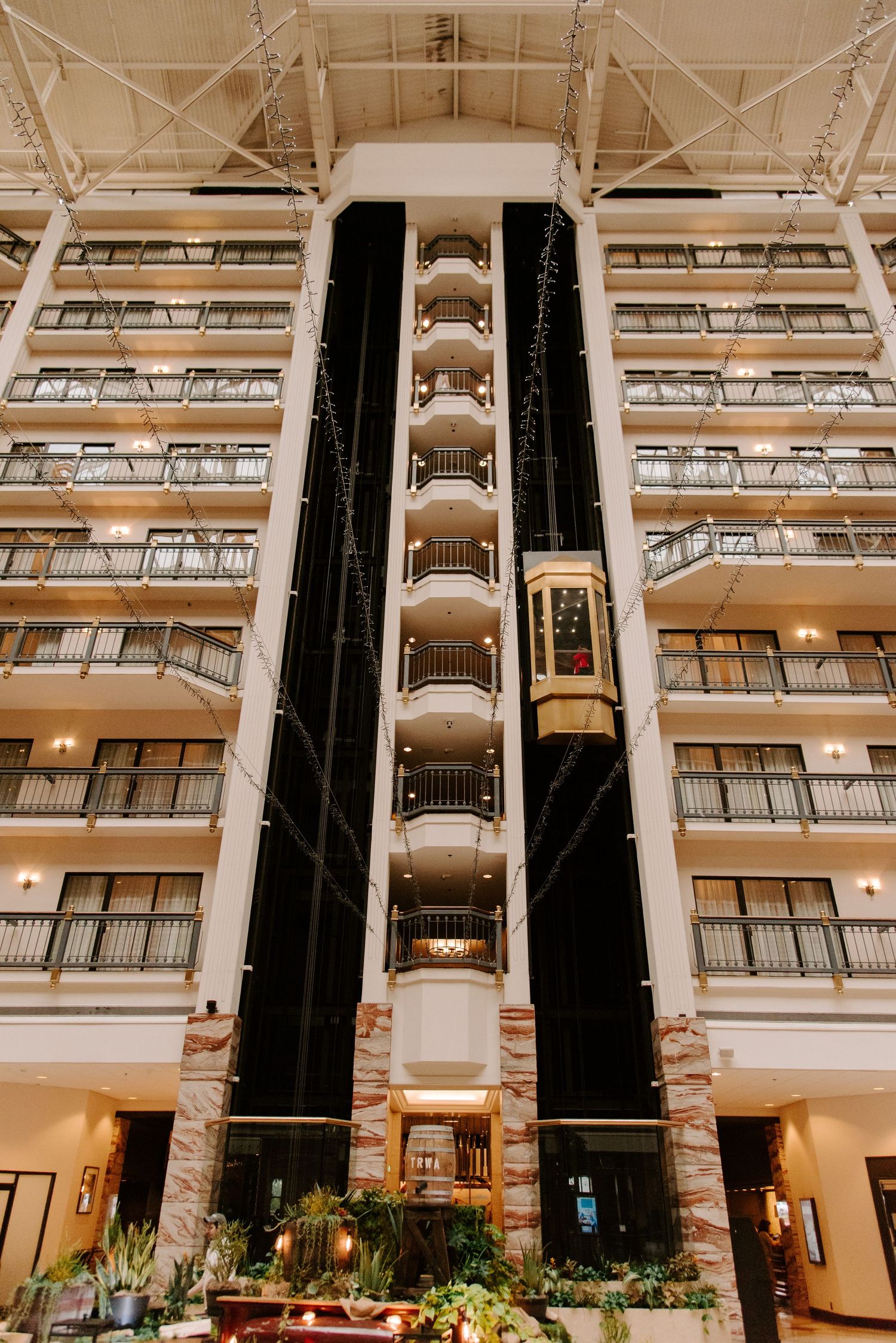 Luxurious hotel atrium with glass elevator shaft and multiple floors of balconies in beige and black architecture.