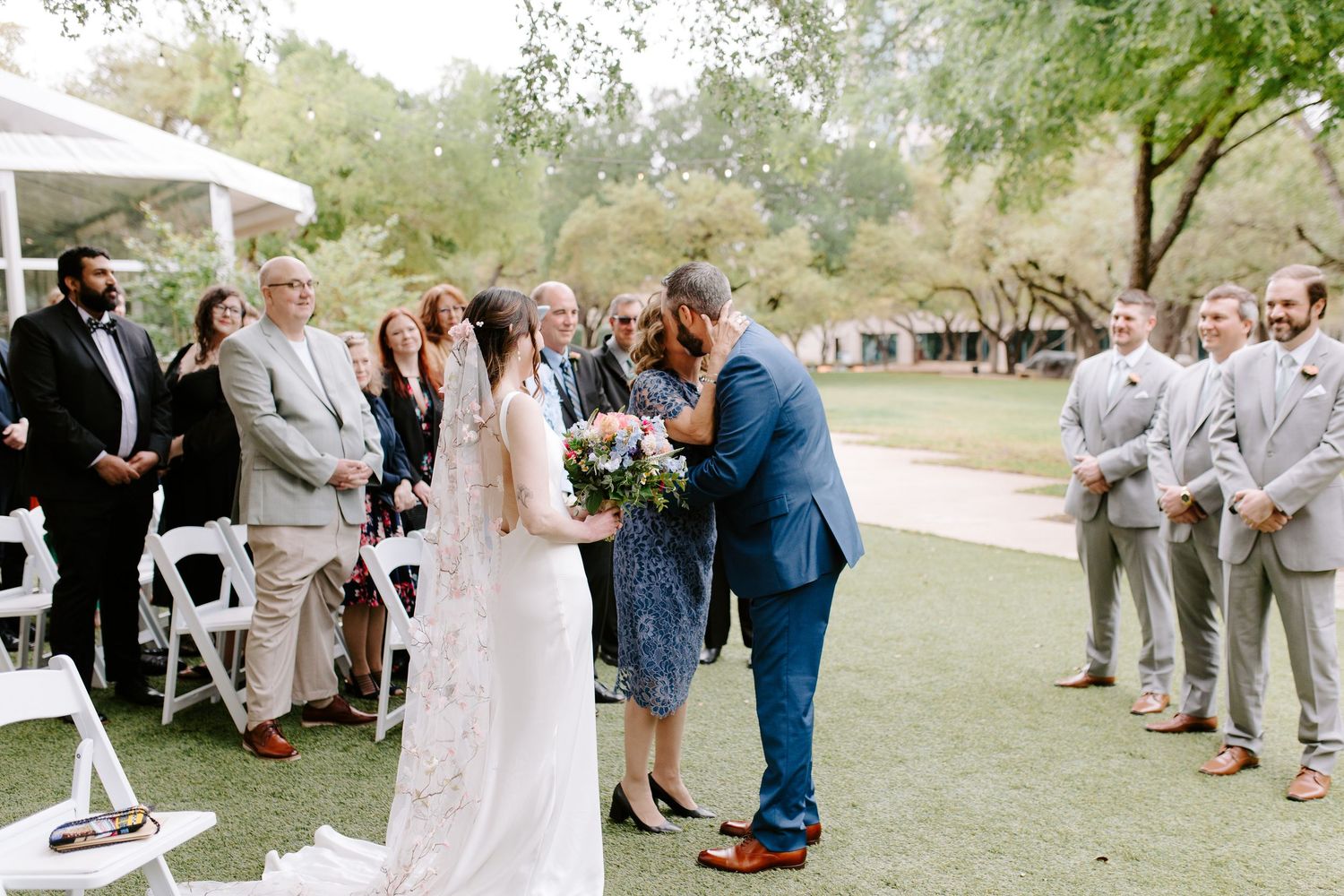 Outdoor garden wedding ceremony with guests gathered on a green lawn watching couple exchange vows.