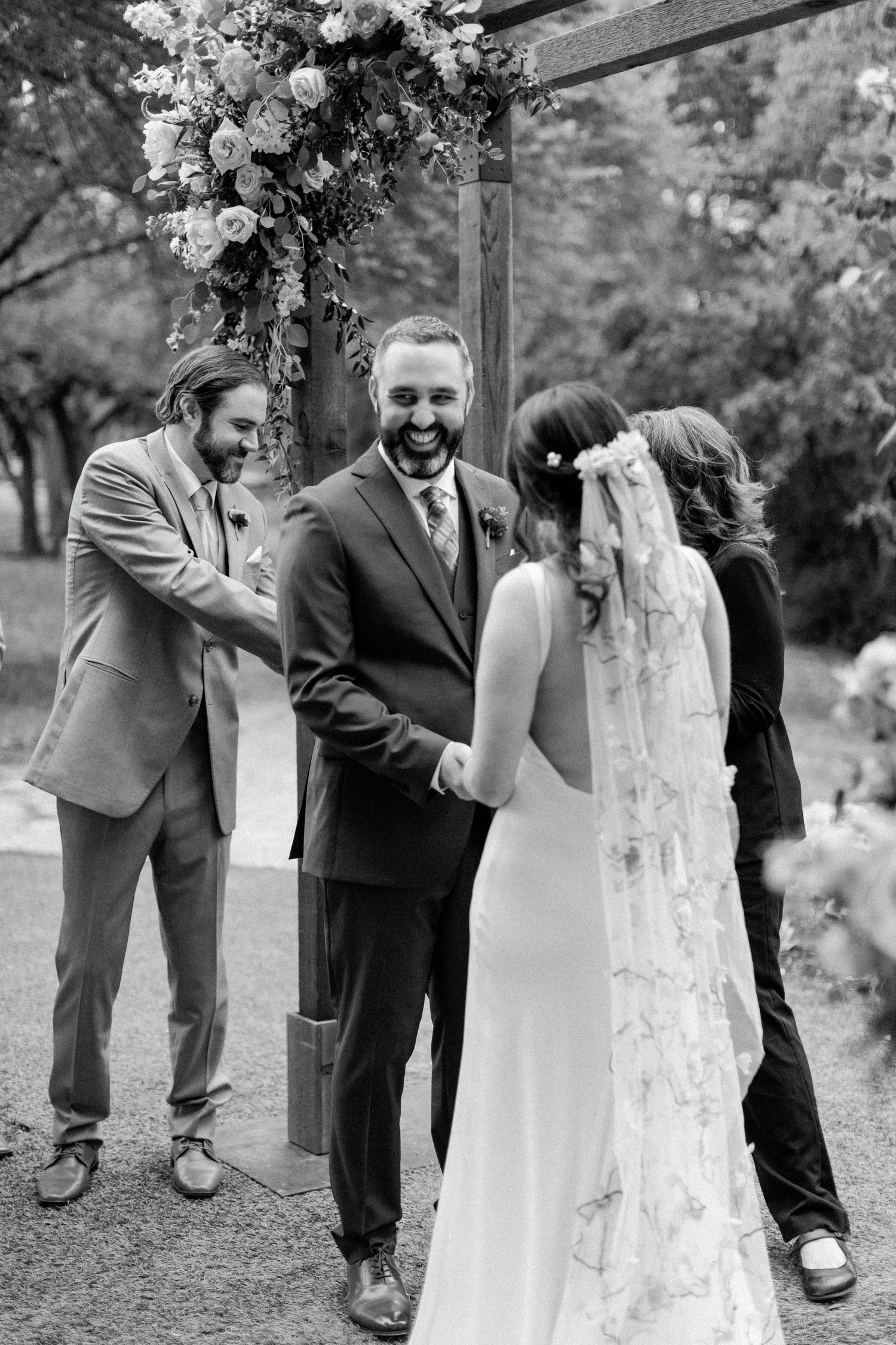 A joyful wedding ceremony takes place under a floral arch as guests share in the couple's happiness.
