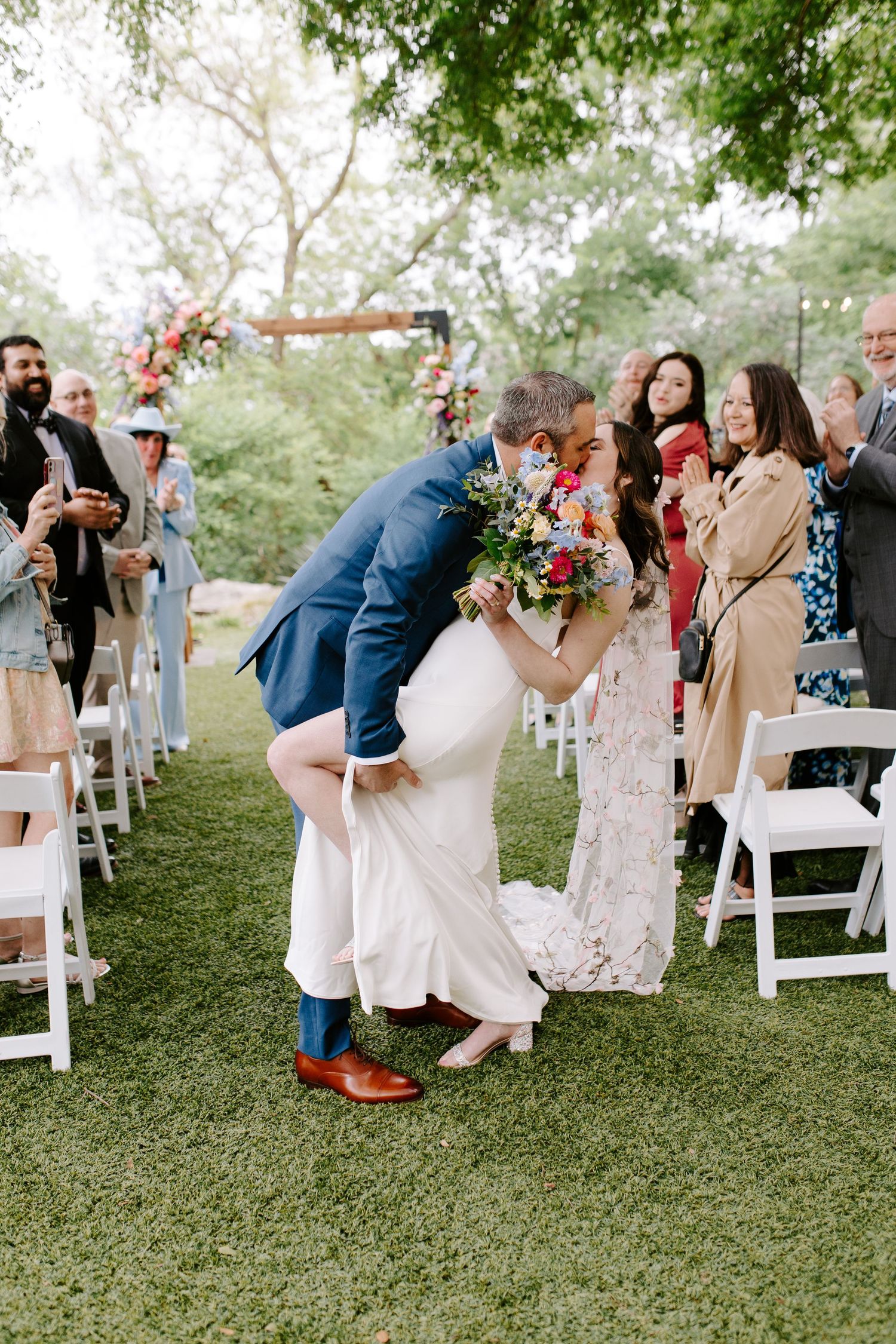 A romantic dip kiss moment during the wedding recessional on a grass-lined aisle.