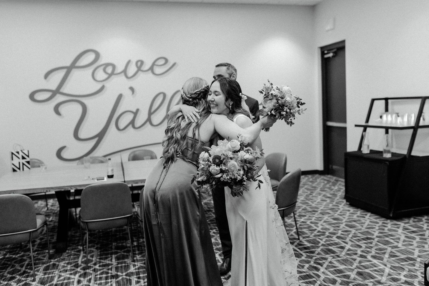 People embracing in a room with a wall decal saying "Love Y'all" in gray script lettering.