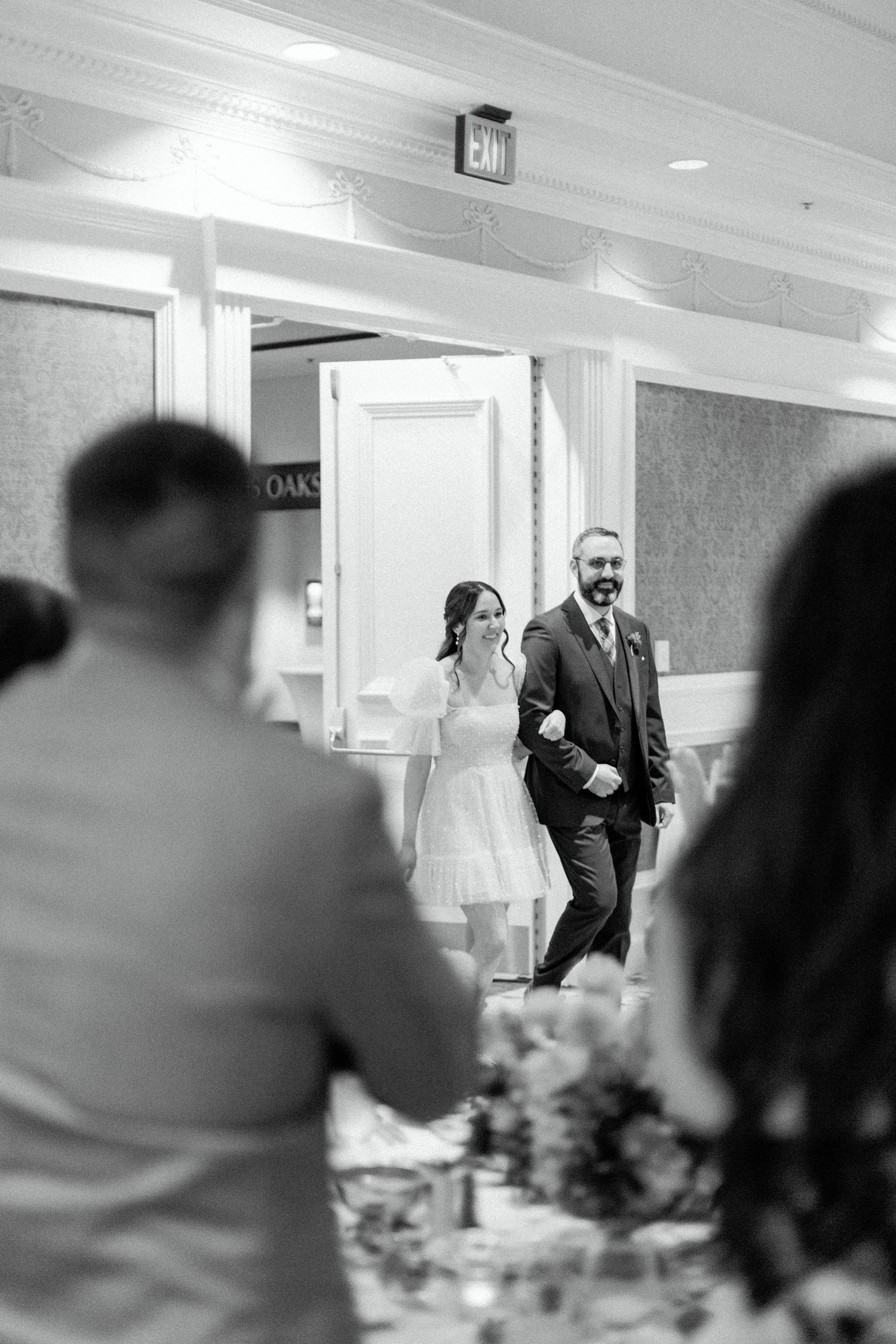 Black and white photo of a wedding entrance into an elegant indoor reception hall.