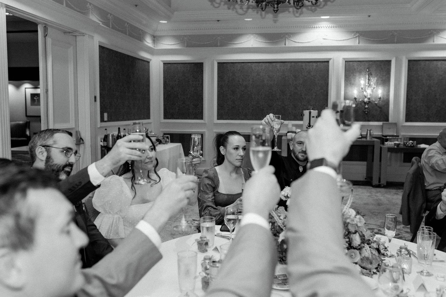 Wedding reception guests raising glasses in a toast during dinner in an elegant ballroom.