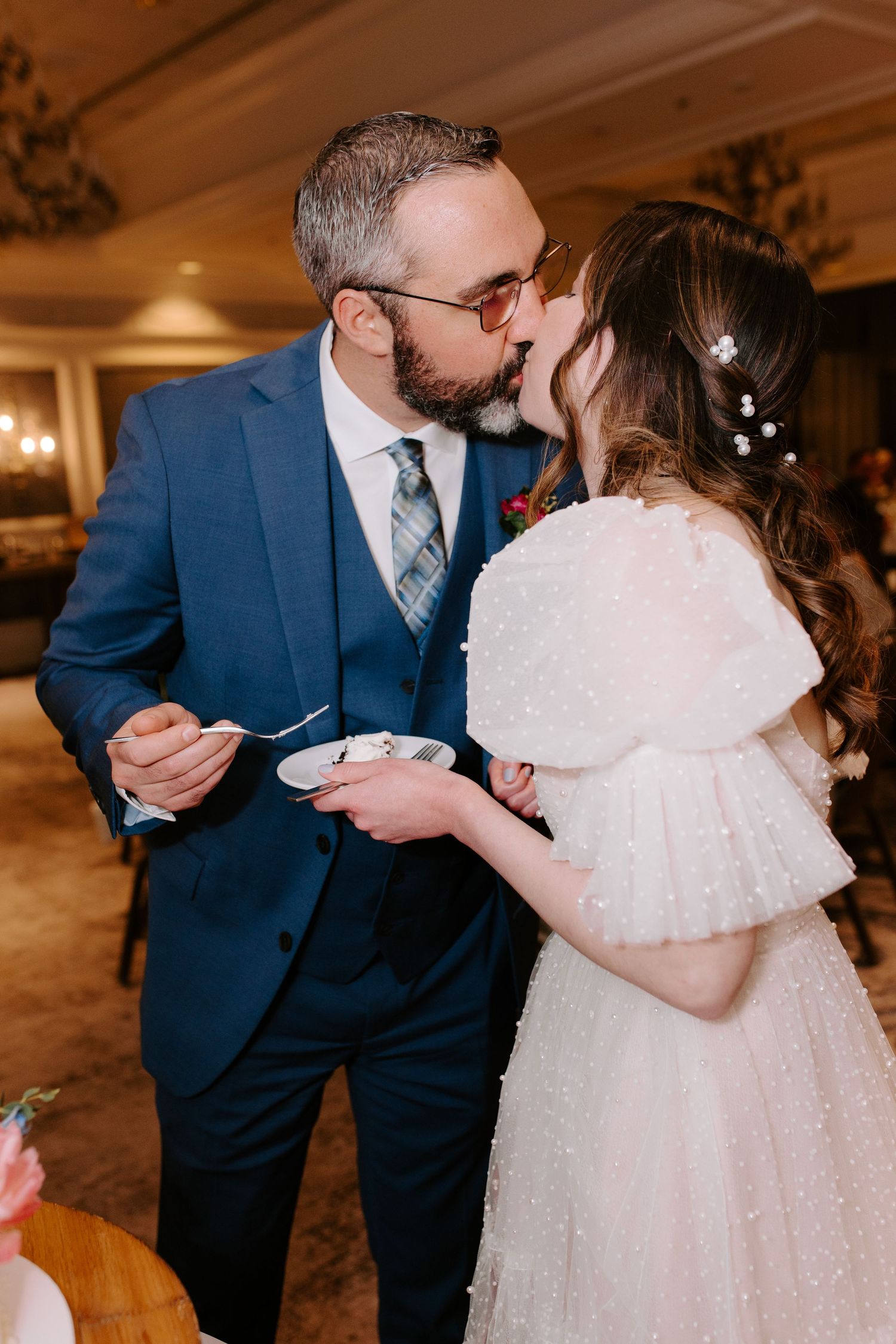 Couple sharing cake during their wedding reception in an elegant ballroom setting.