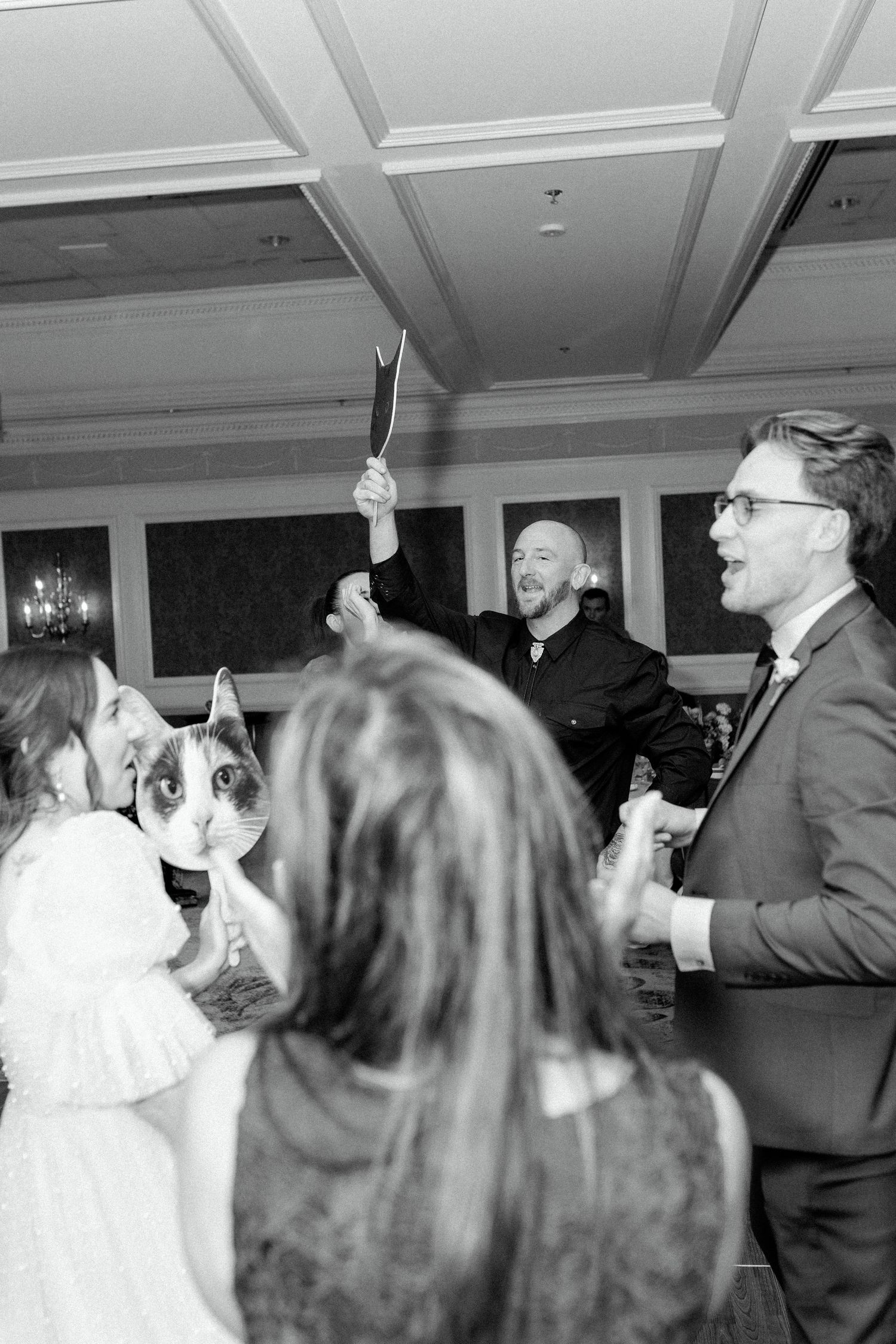 Wedding celebration with guests dancing and raising champagne glasses in a grand ballroom.