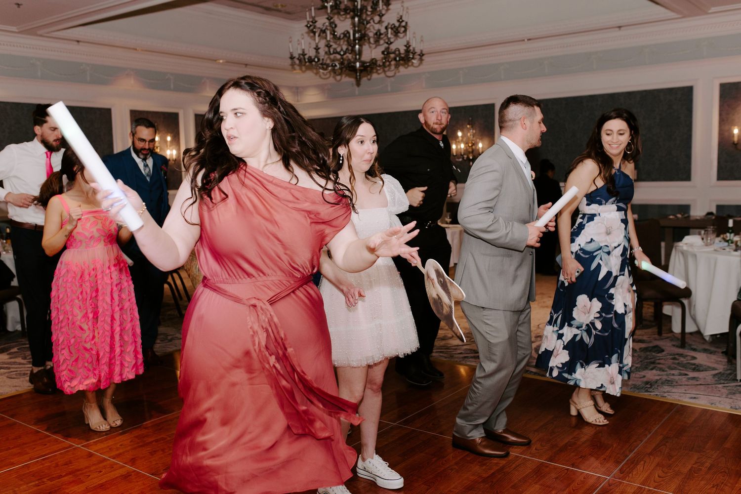 Wedding guests dancing and celebrating on a wooden dance floor under an elegant chandelier.