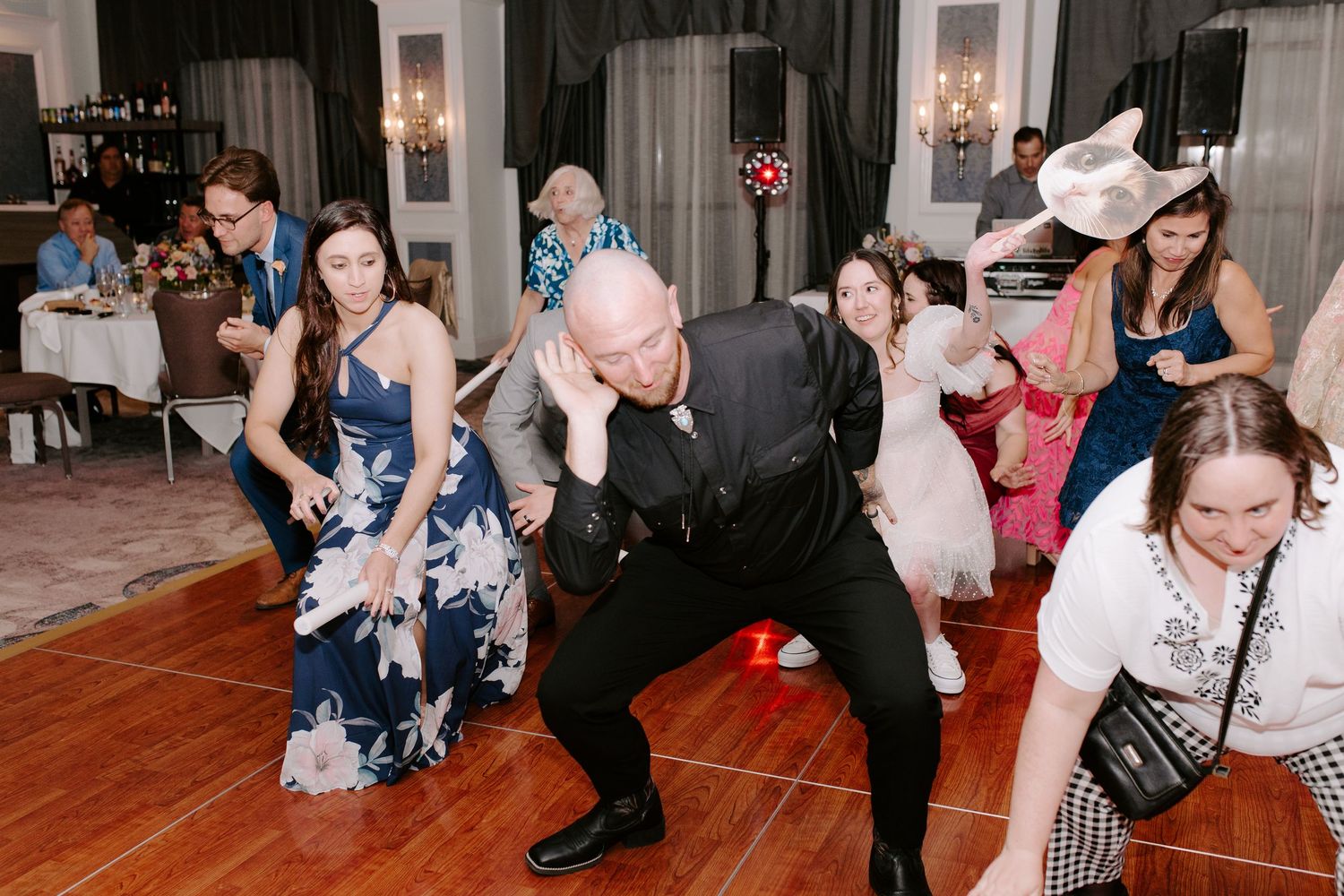 Group of wedding guests dancing energetically together on a wooden dance floor at a reception celebration.
