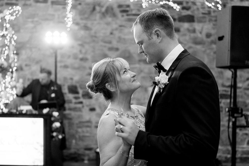 A tender moment between a bride and groom during their first dance at a rustic stone venue reception.