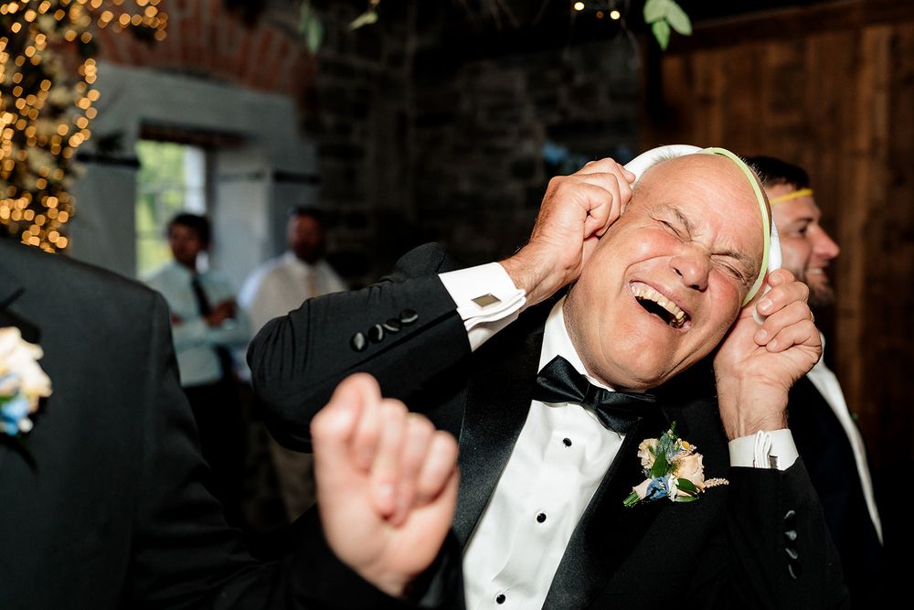 Someone in a tuxedo laughs joyfully at a formal event while wearing a boutonniere and black bow tie.