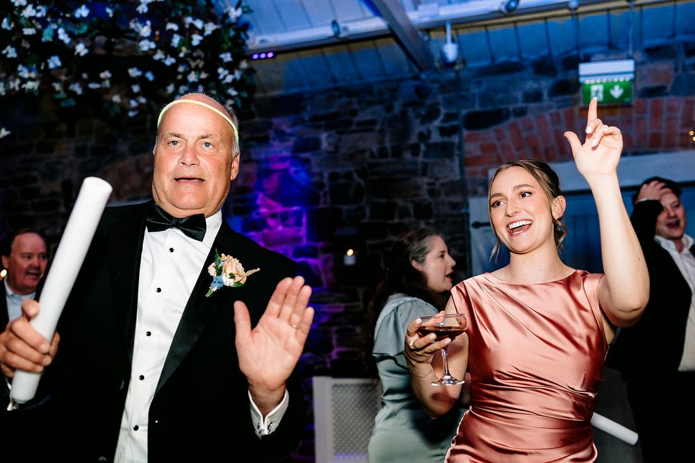 Celebrants dancing energetically on a dance floor illuminated with blue lighting at an evening event.