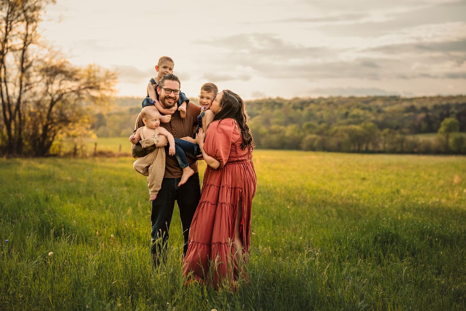 A family stands together in a sunlit meadow at sunset, surrounded by rolling hills for family photos by Chattanooga photographer.