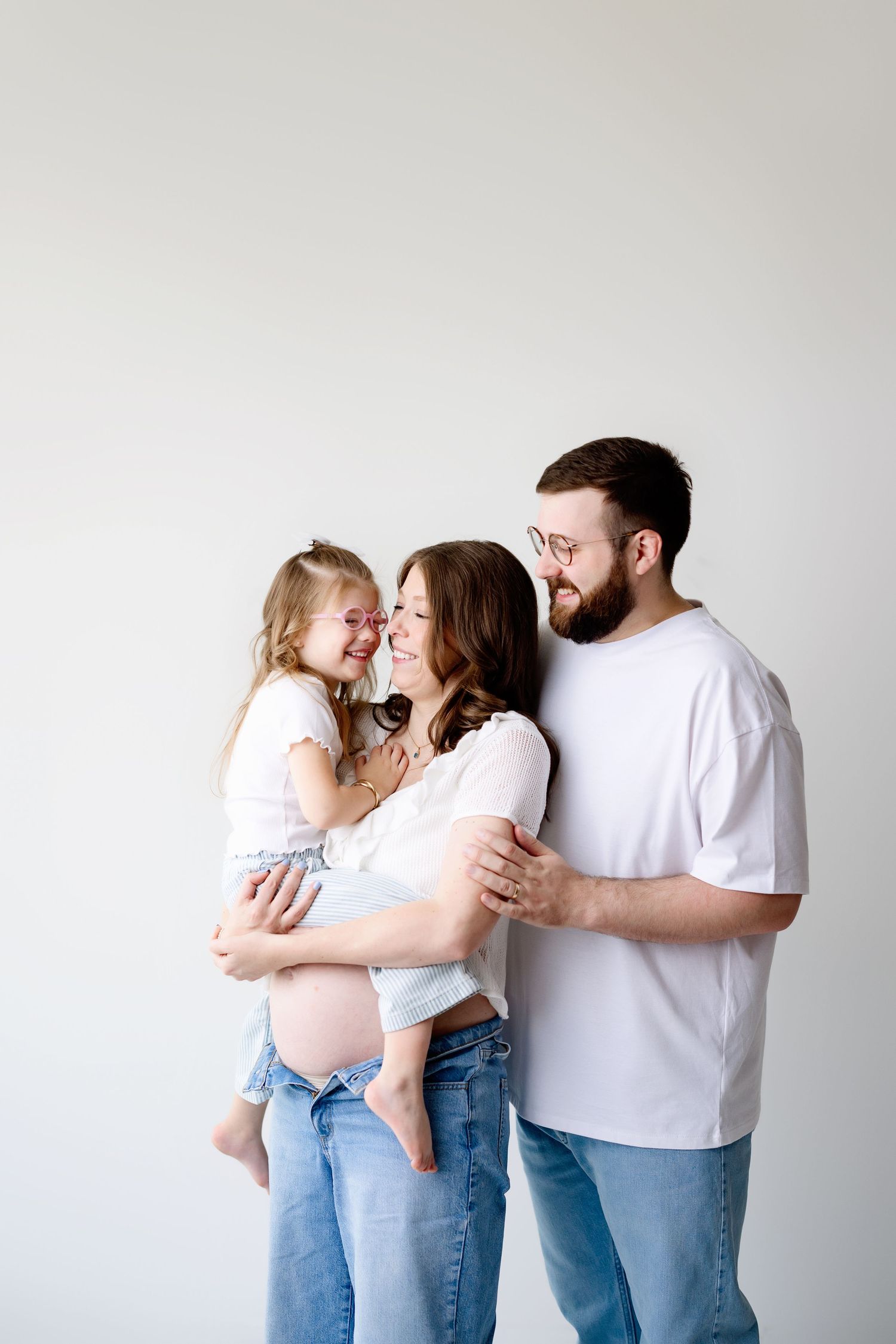 A joyful family portrait against a white wall shows tender embraces and laughs between parents and child.
