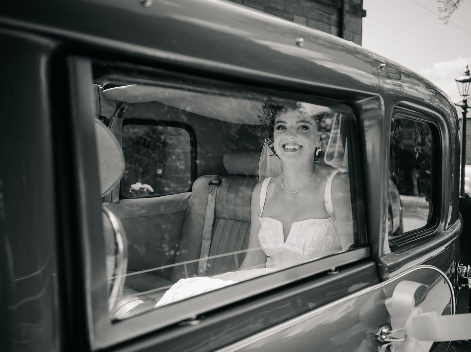 A vintage 1930s car with passengers visible through the window in a black and white photograph.