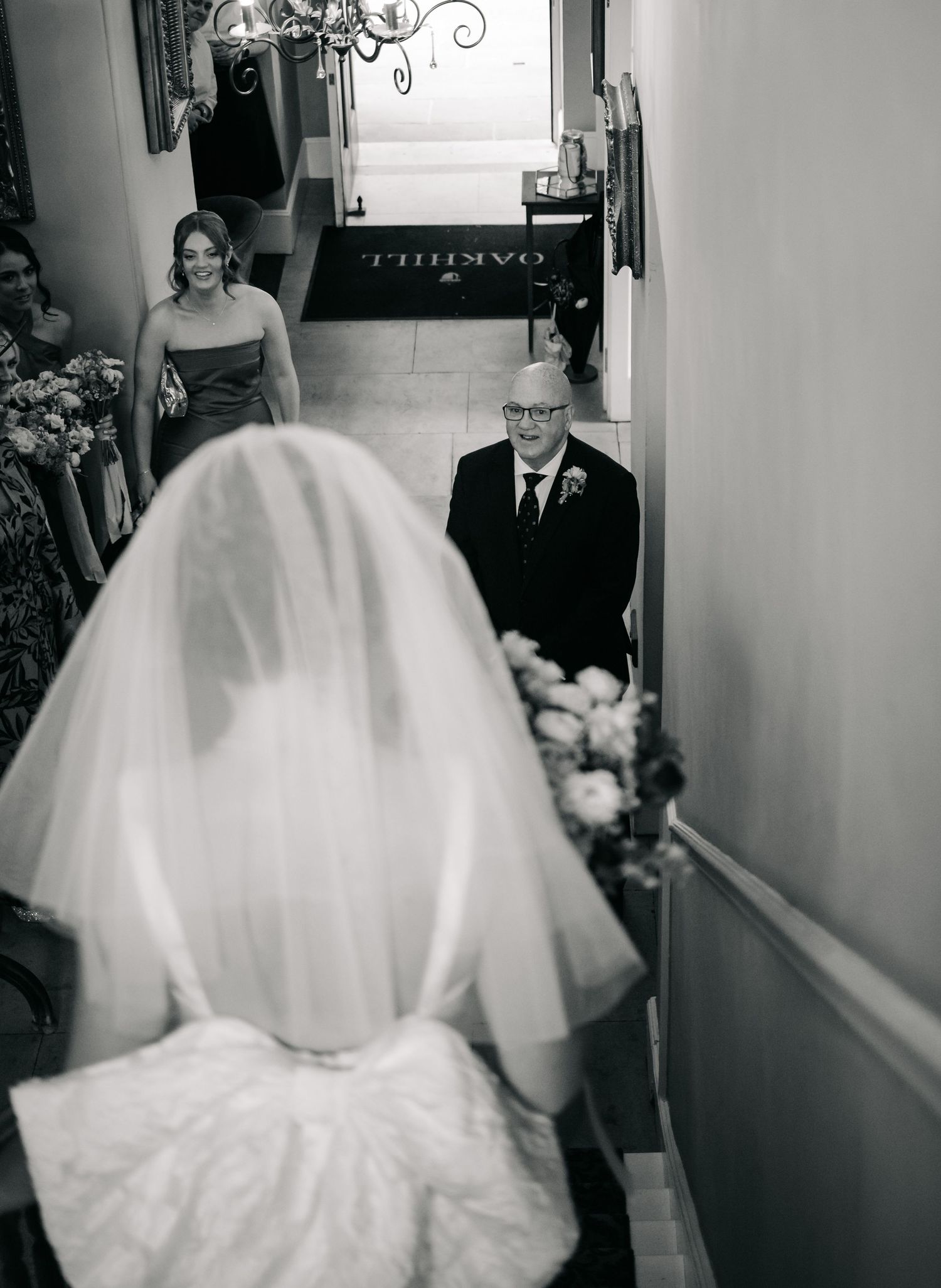 A poignant black and white photo captures a private wedding moment on stairs with guests and a bride in flowing veil.