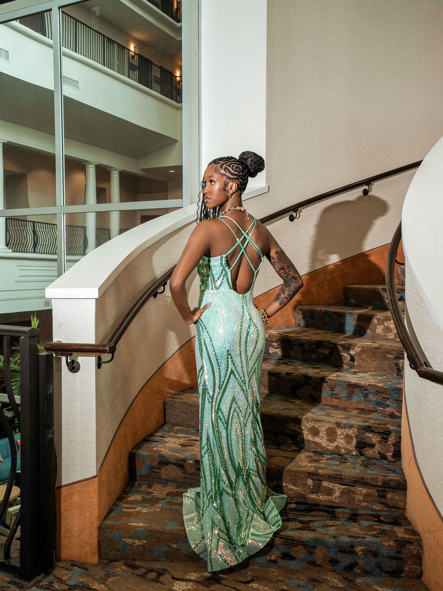 Elegant mint green sequined gown with strappy back detail shown on curved staircase in formal venue.