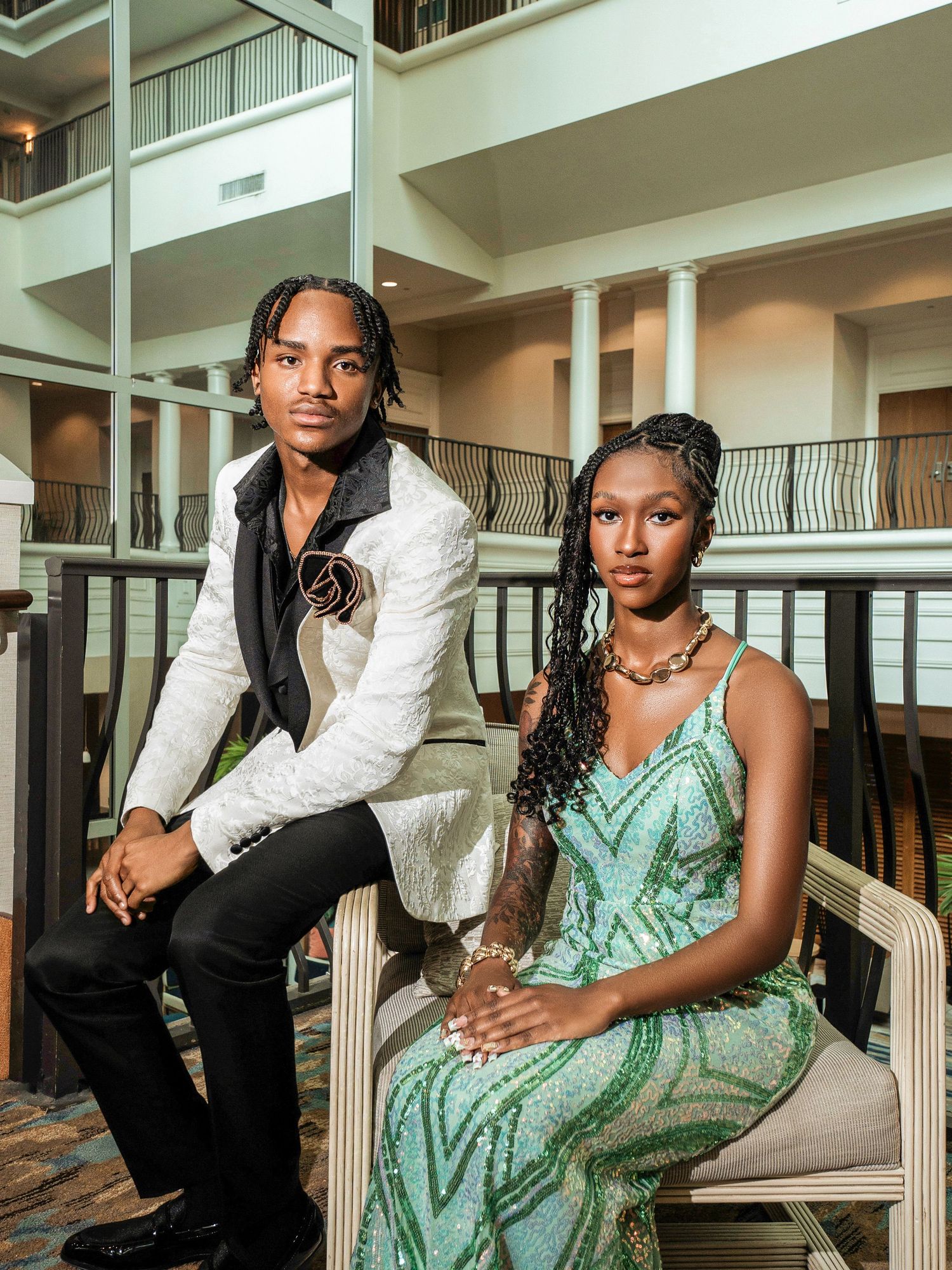 A formal portrait shows two people posed elegantly on indoor seating, wearing white blazer and mint green dress.