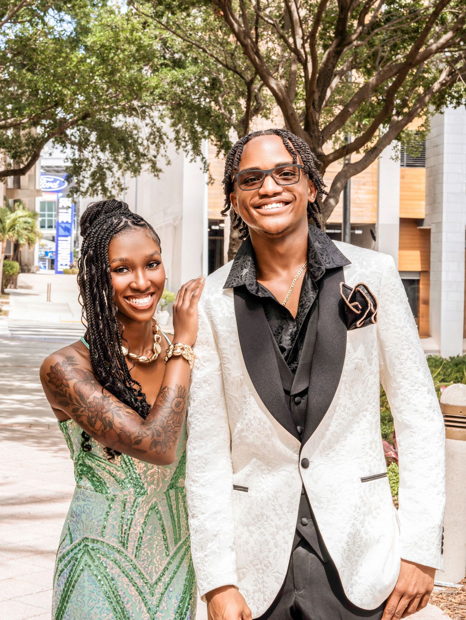 A couple smiles together outdoors wearing elegant formal wear with a white jacket and mint green sequined dress.