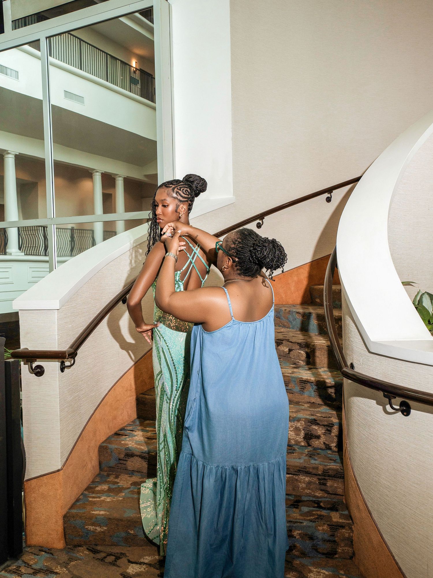 Two people sharing an embrace on a carpeted staircase with a white railing in an interior setting.