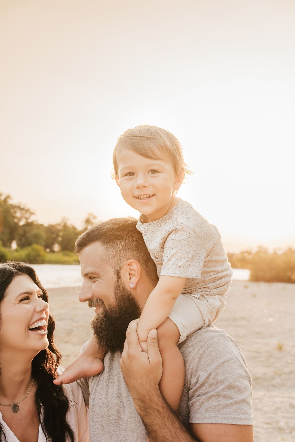 little boy sits on dad's shoulders as family plays near river outside of cincinnati, ohio