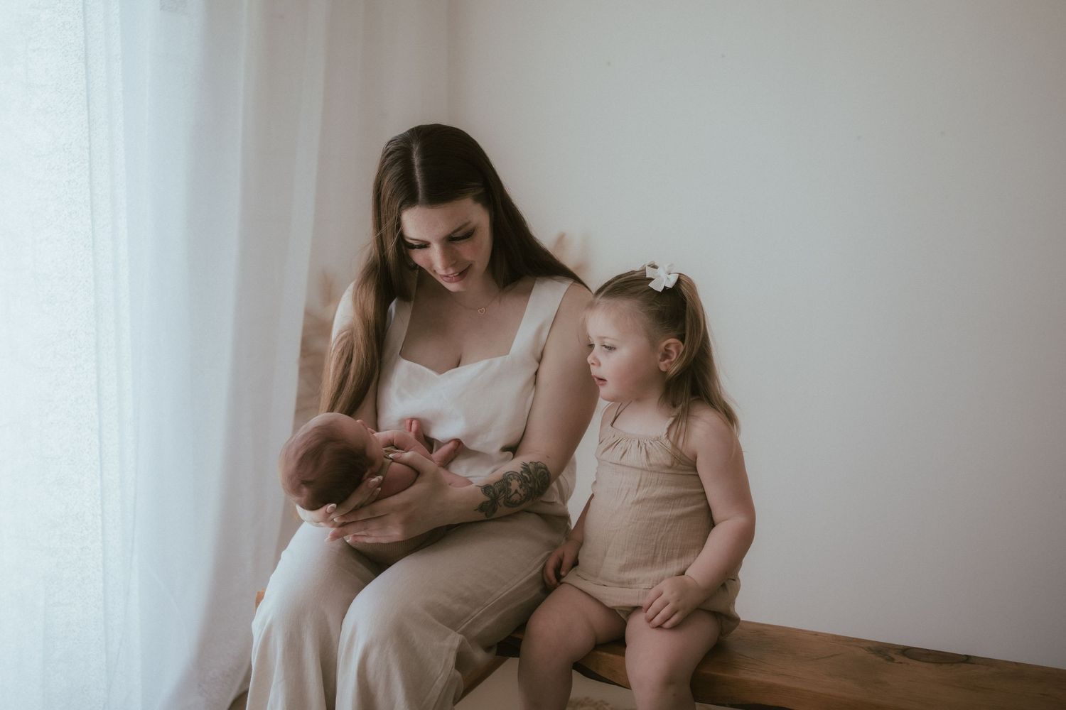 A tender moment of breastfeeding and bonding between parent and children beside a bright window.