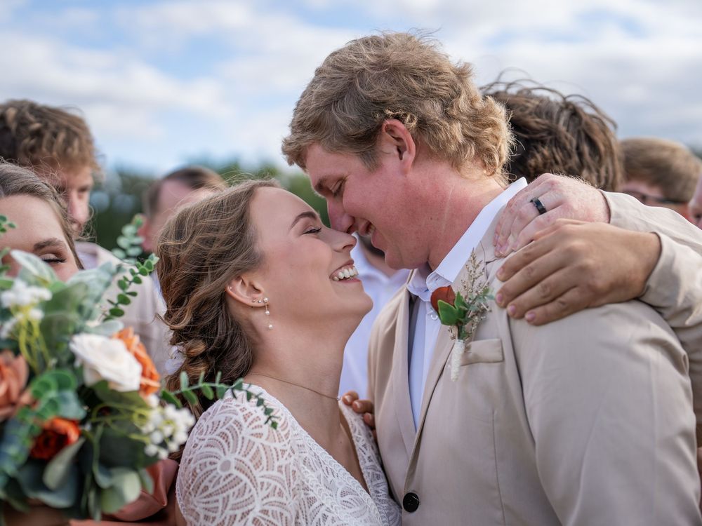 Joyful couple sharing an intimate moment during their wedding ceremony with orange floral bouquets and sunny skies.