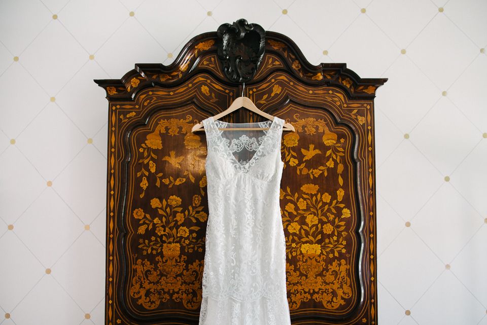 White lace wedding dress hanging on vintage wooden armoire with ornate floral marquetry design.