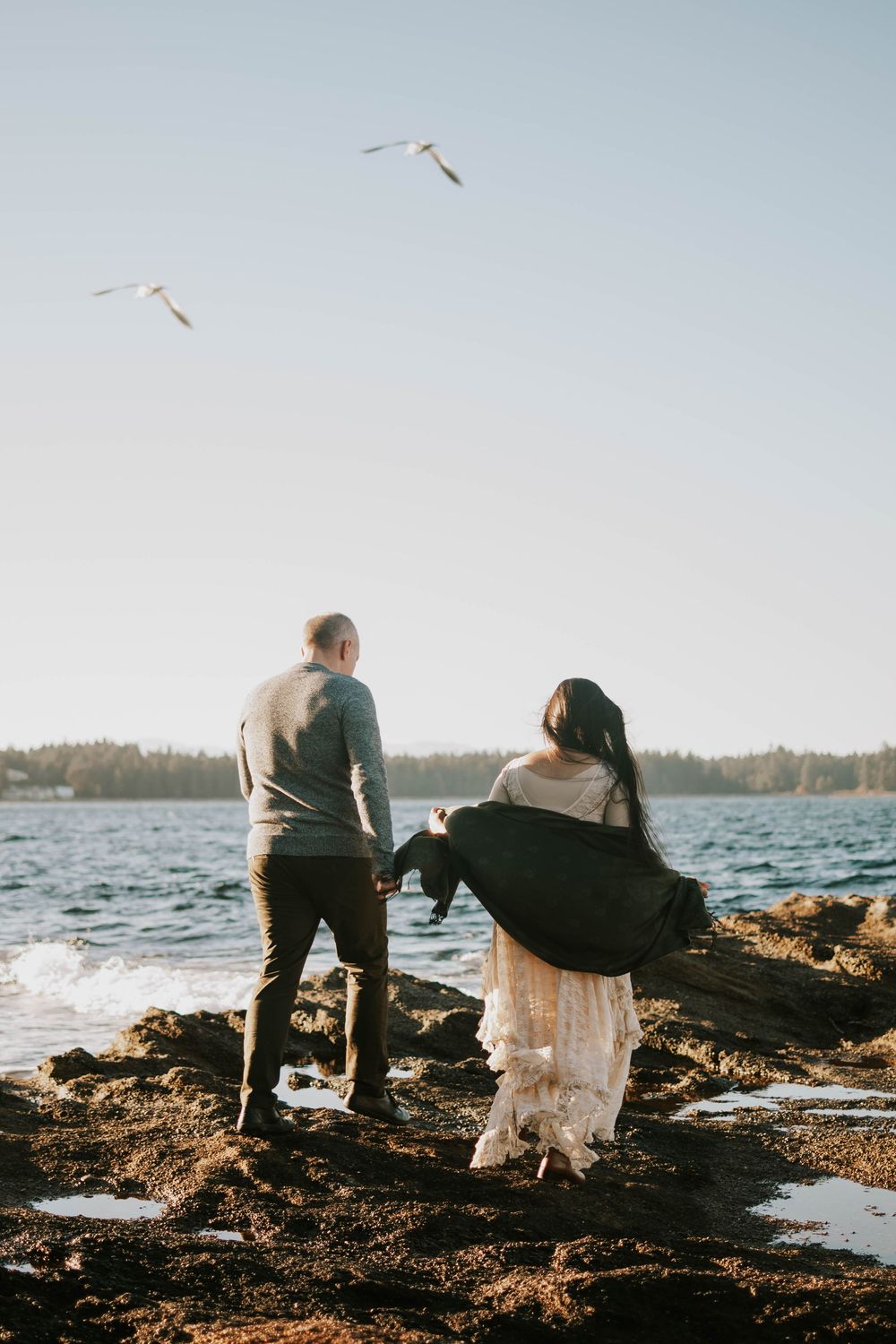 Parksville photography portrait of couple walking along Madrona Point Beach on rocky shore on Vancouver Island birds, and sunset photoshoot