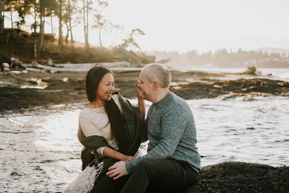 Parksville photography portrait of couple sitting along Madrona Point Beach on rocky shore on Vancouver Island sunset photoshoot