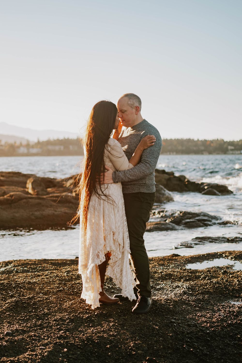 Beautiful image taken at Madrona Point Parksville Vancouver Island of couple hugging on beach shore during sunset photoshoot