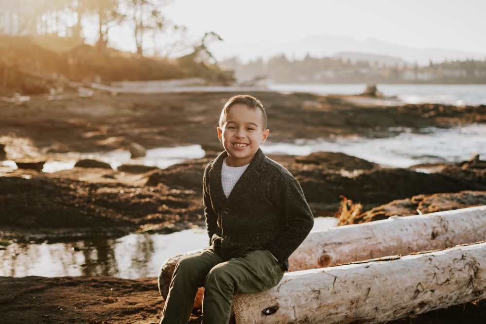 Parksville photographer portrait of young son sitting during family photoshoot at Madrona Point Beach on rocky shore on Vancouver Island