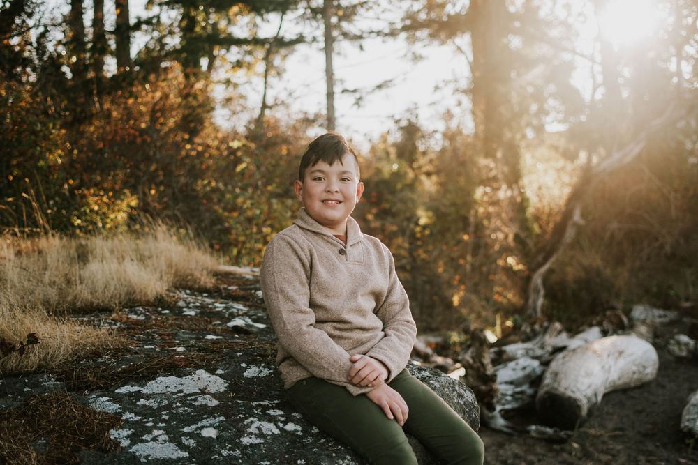 Parksville photographer portrait of young son sitting during family photoshoot at Madrona Point Beach on rocky shore on Vancouver Island