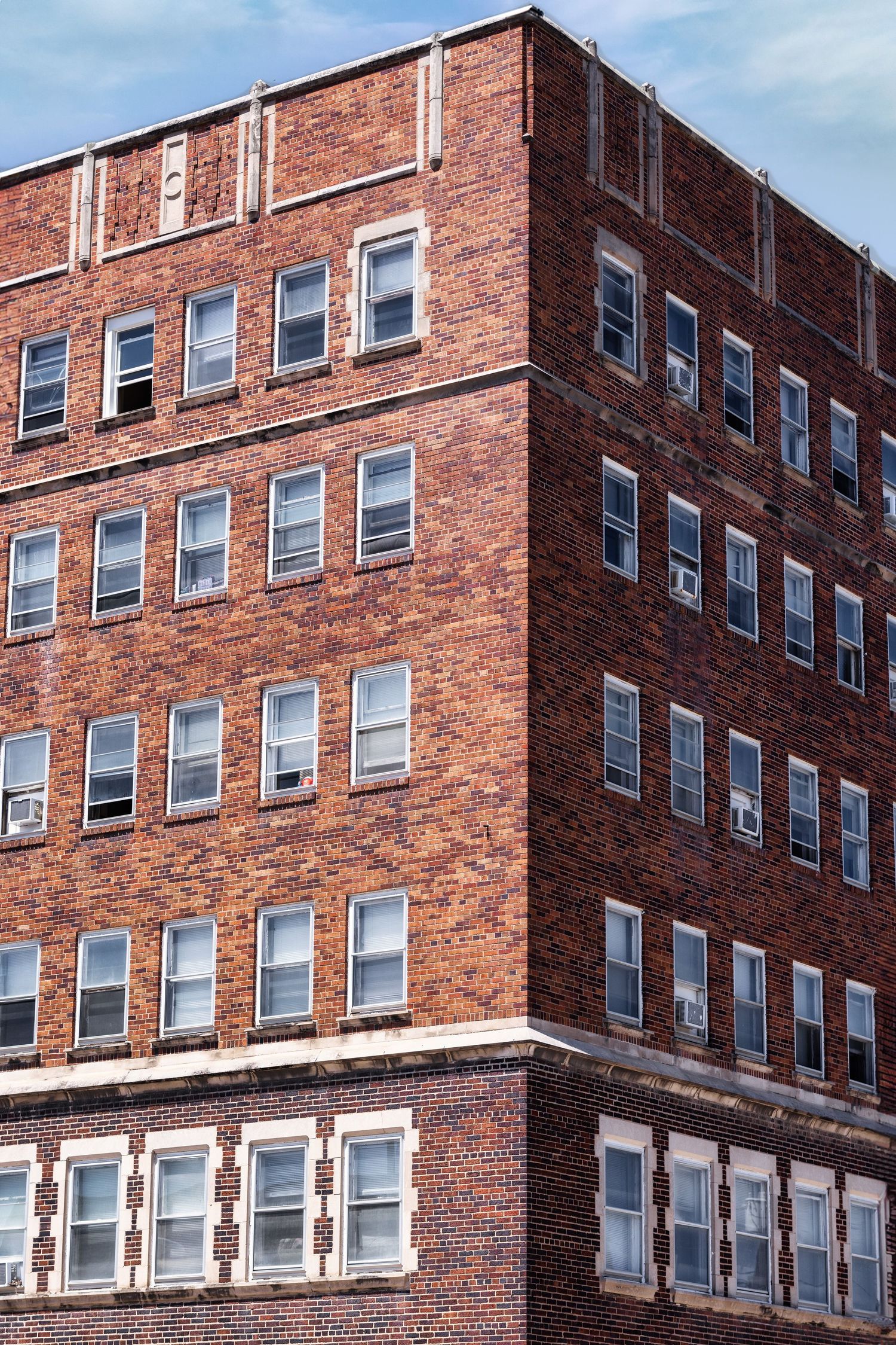 Exterior detail of a red brick apartment building with white-trimmed windows showing multiple stories under blue sky.