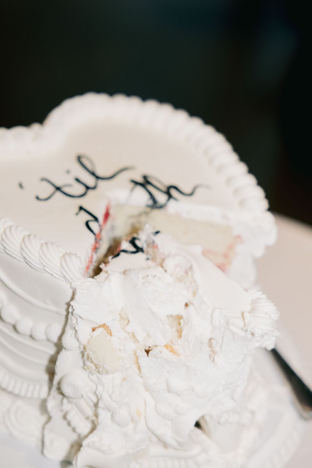 A white wedding cake with classic piped frosting details and partially damaged frosting decoration on top.