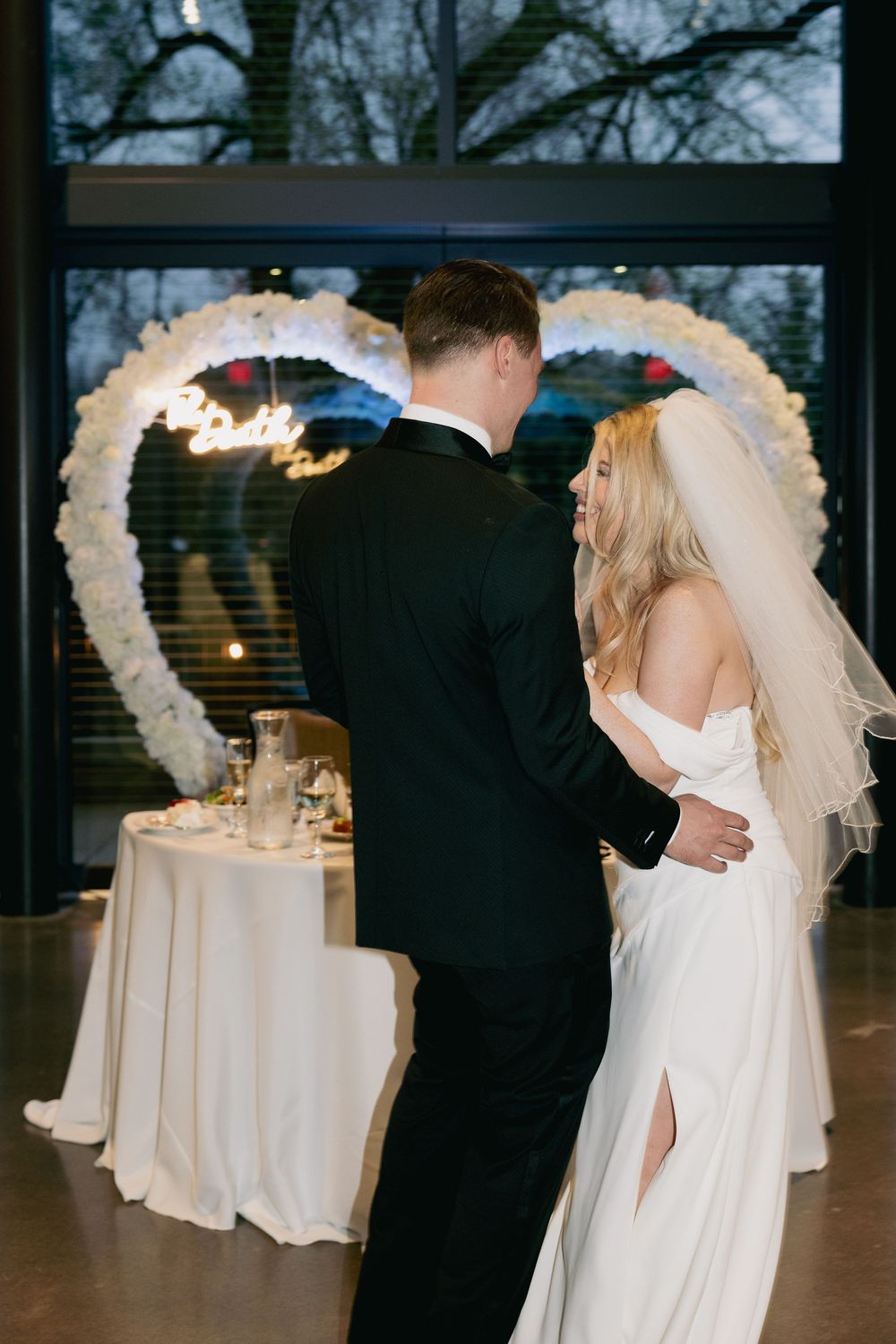 A couple shares an intimate moment at their wedding reception in front of a decorative heart-shaped light display.