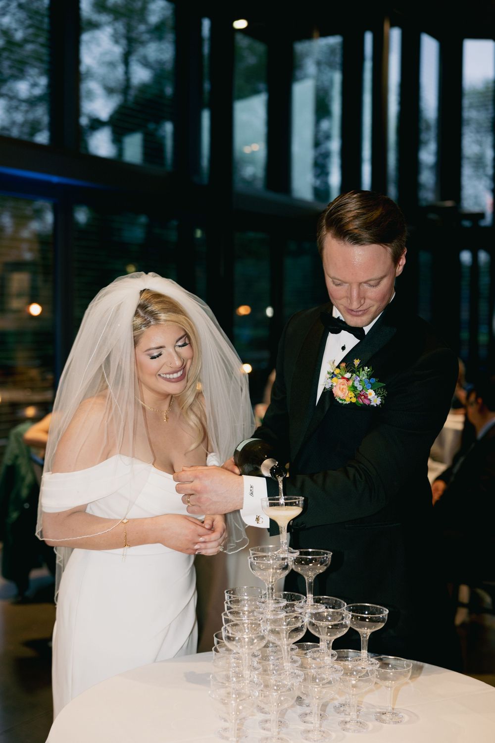 A couple pours champagne into a tower of glasses at their elegant wedding reception.
