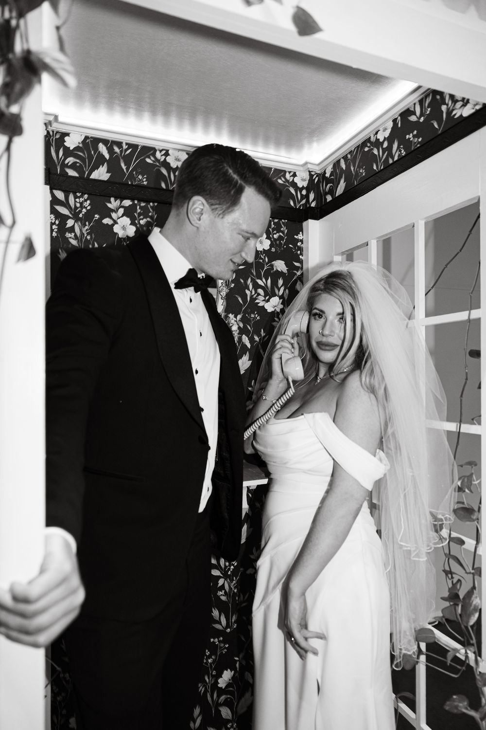A black and white wedding photograph showing a bride in white dress and veil with her groom in a tuxedo.