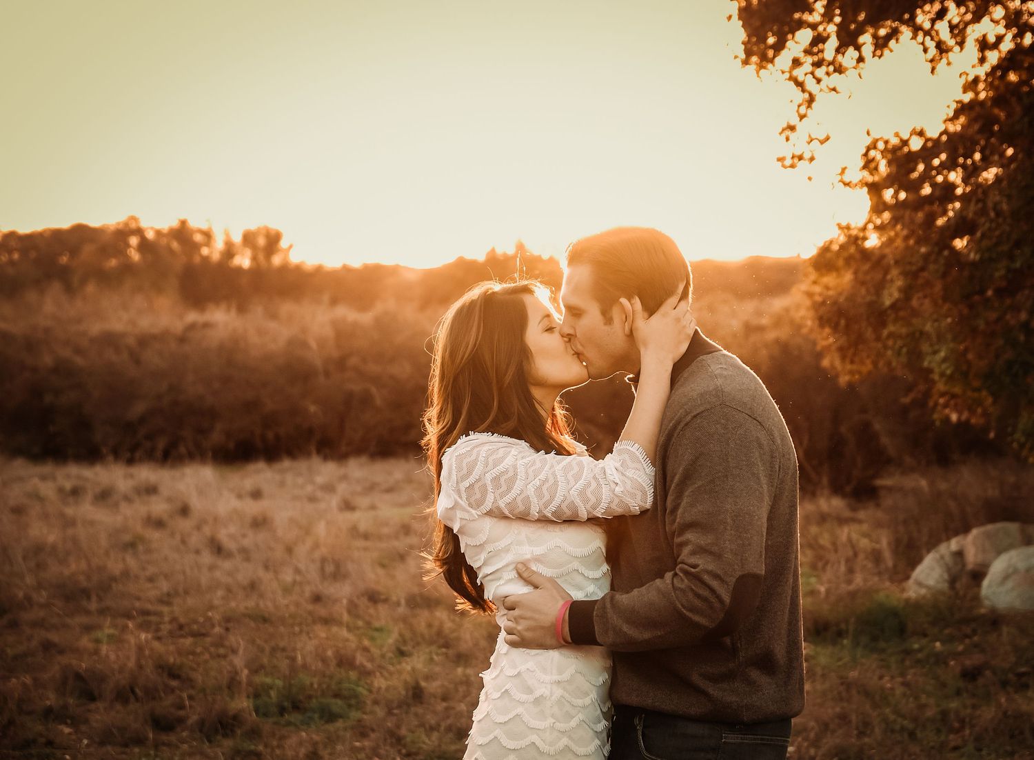 A couple embraces in a warm autumn field during golden hour as the sun sets behind them creating a romantic silhouette.