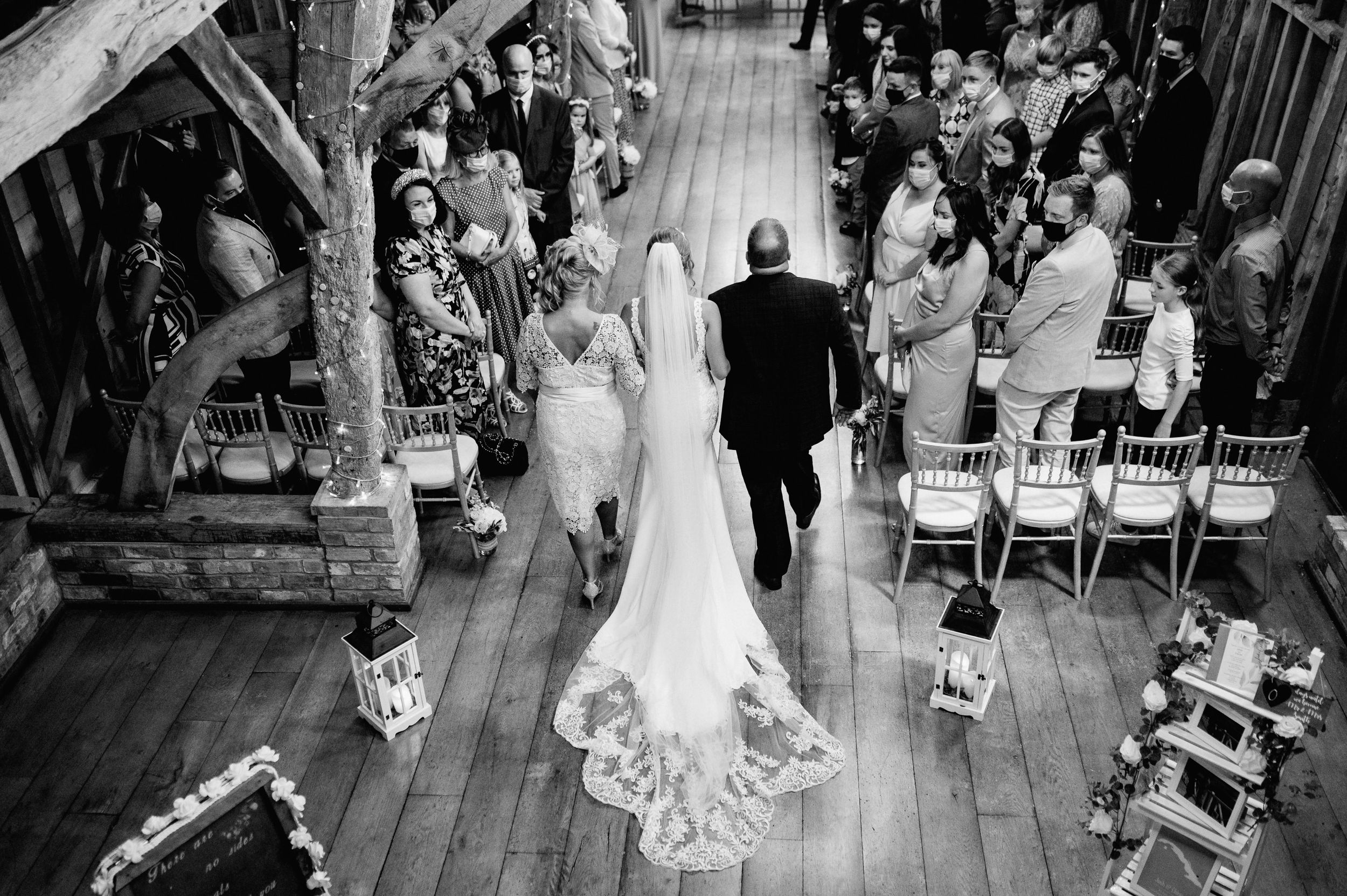 Black and white wedding ceremony processional in wooden barn venue with guests seated.