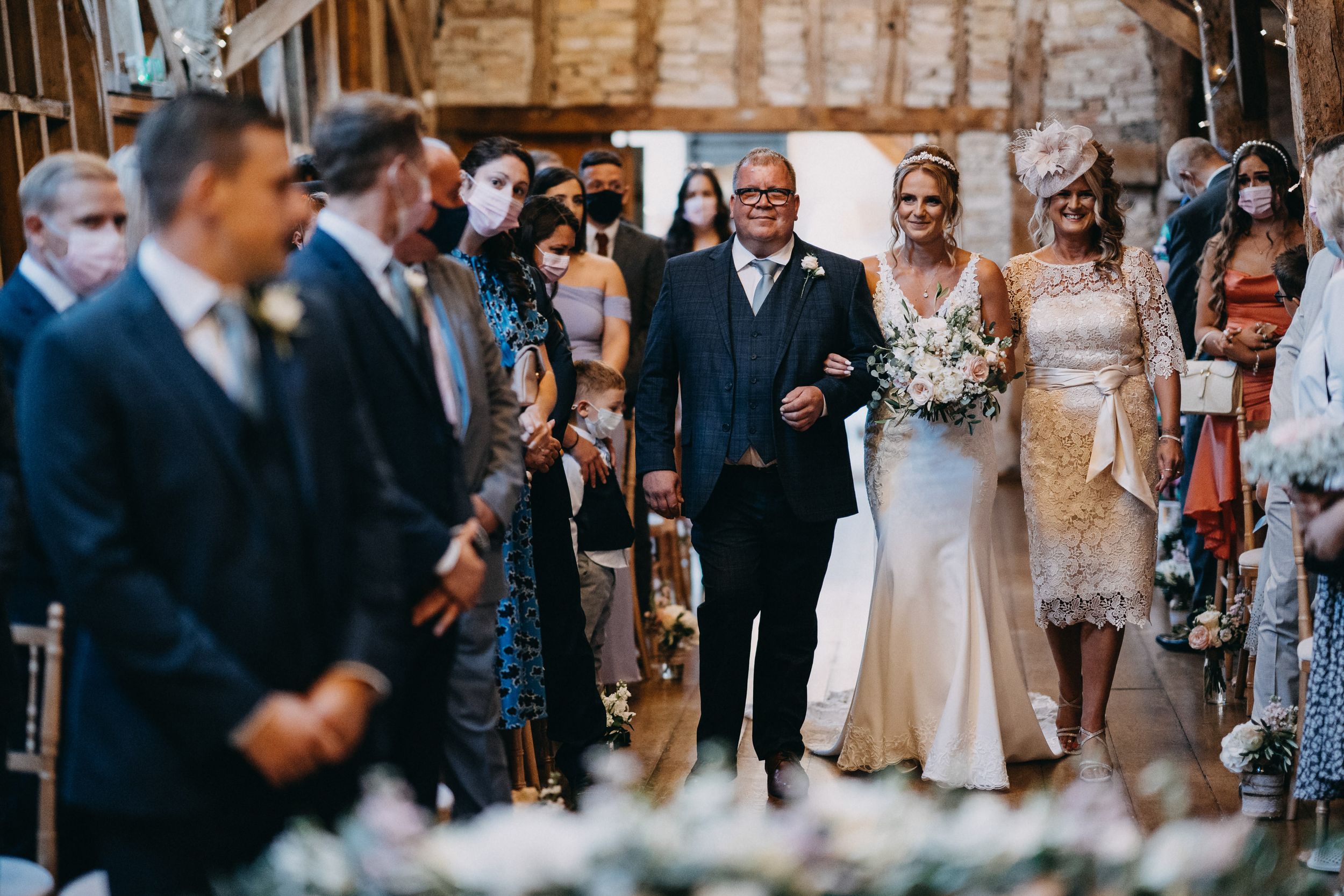 Wedding ceremony in rustic barn of Bassmead Manor Barns venue with guests watching the processional.