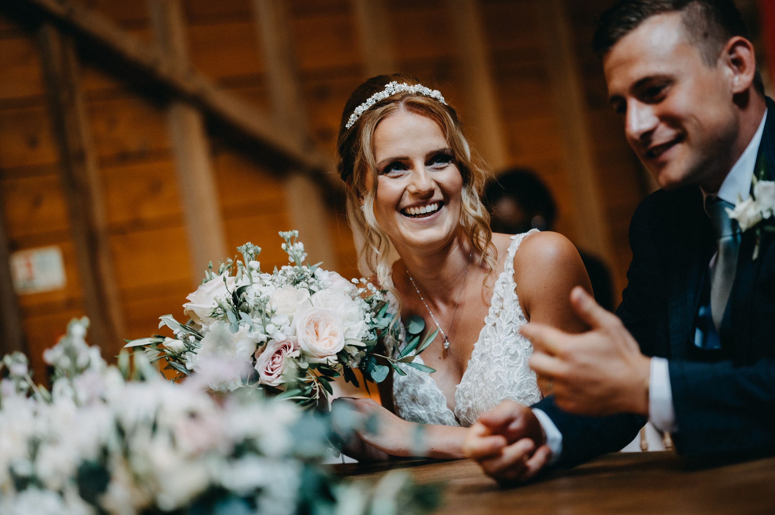 A joyful wedding celebration moment captured in a rustic wooden barn setting with white floral arrangements.